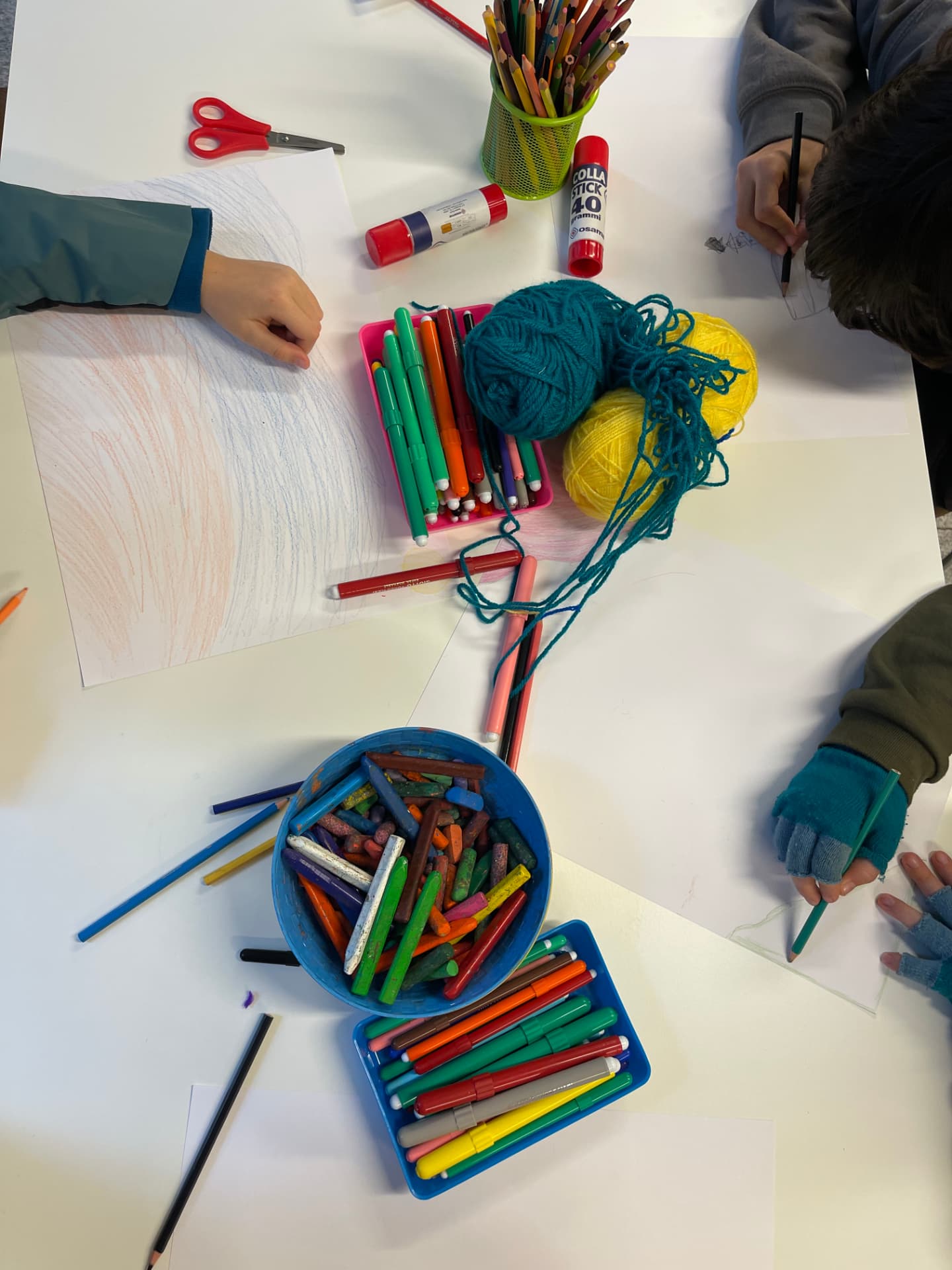 Manos de niños dibujando con lápices, ceras y lanas sobre la mesa