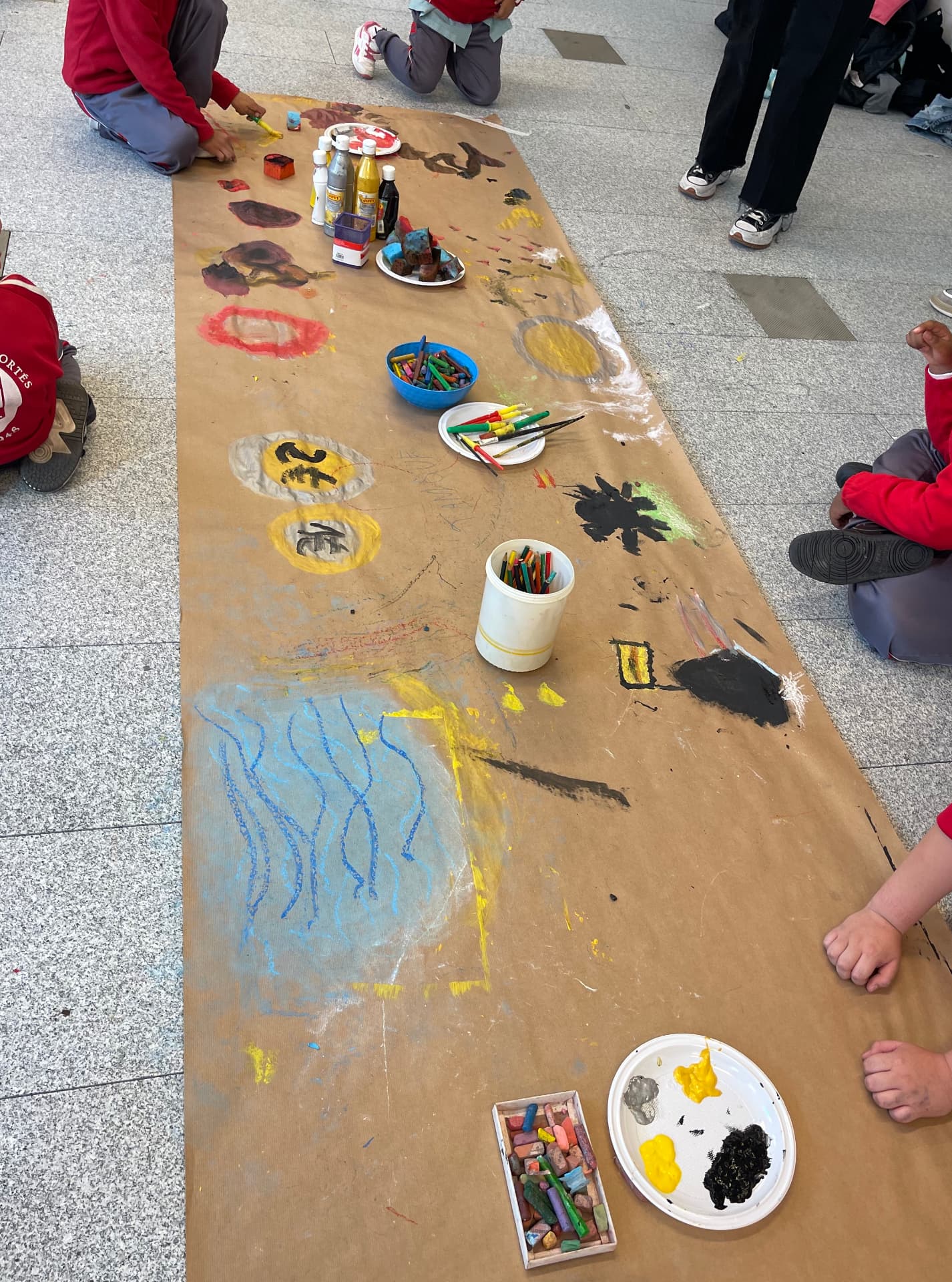 Pintura grupal sobre un gran papel en el suelo con témperas y ceras